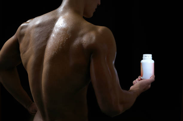 Homme musclé de dos qui tient un flacon de compléments alimentaires